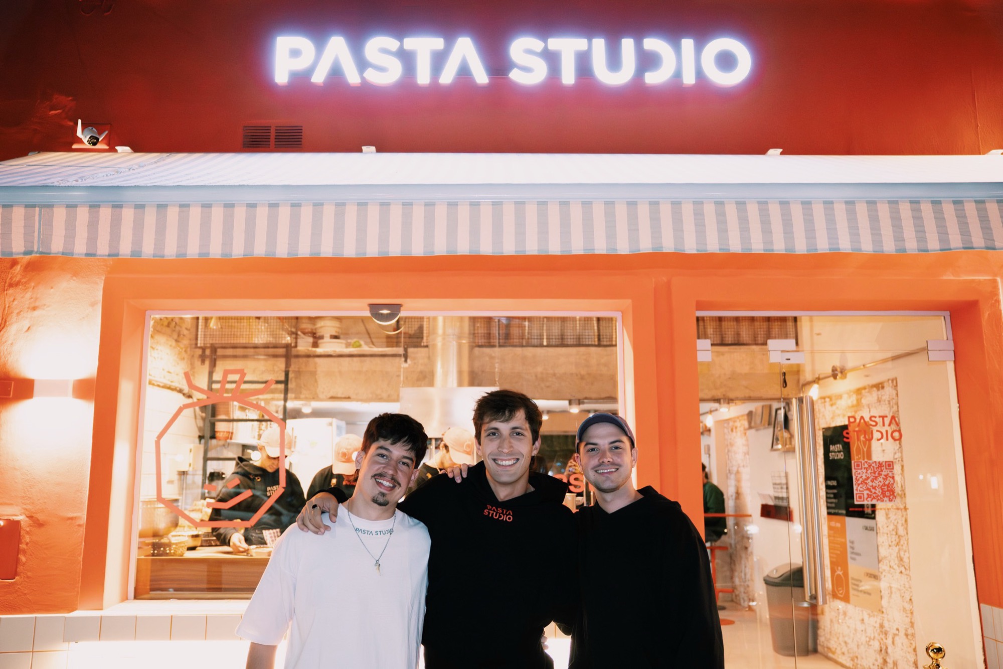 Fachada de Pasta Studio en Jesús María de noche, con el cartel iluminado y el equipo en la puerta