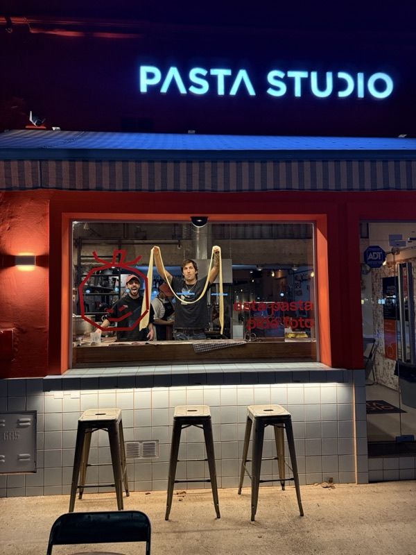 Fachada de Pasta Studio de noche: el equipo estira pasta fresca en la ventana de la cocina a la vista