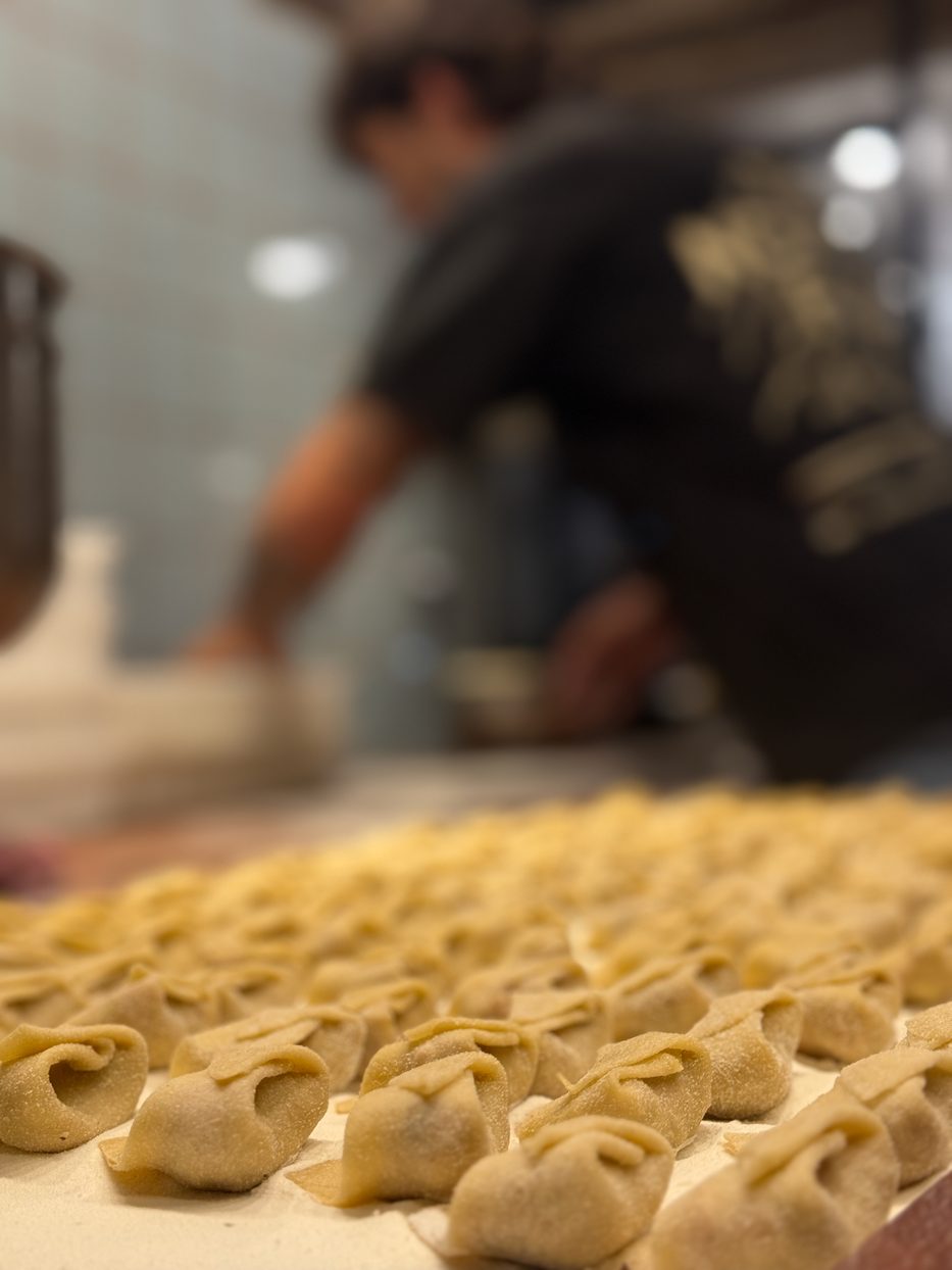 Sorrentinos recién armados en primer plano y un cocinero de Pasta Studio trabajando detrás